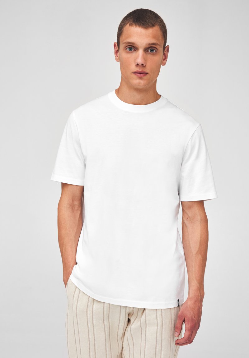 T-shirt en coton blanc avec un col rond et des manches courtes, présentant une coupe droite et un design minimaliste.
