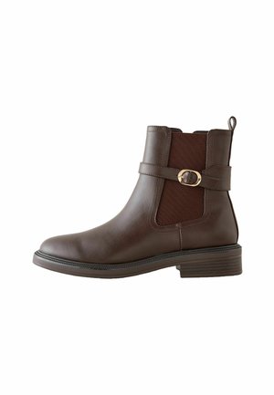 Bottine en cuir marron avec des panneaux élastiques sur les côtés, bout rond et une sangle décorative avec boucle dorée. Semelle texturée avec un talon modeste.