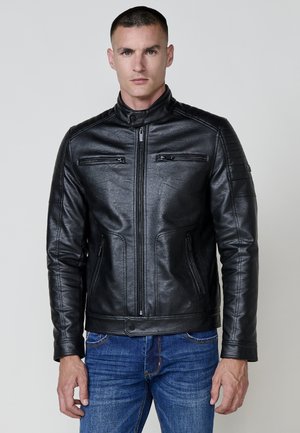 Chaqueta de cuero negra con un alto cuello, frontal con cremallera y dos bolsillos en el pecho. Presenta detalles texturizados en los hombros y un diseño ajustado.
