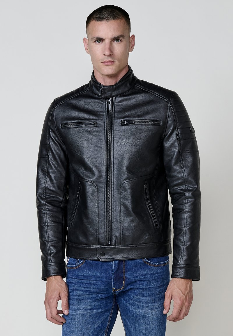 Črna usnjena jakna z visokim ovratnikom, zadrgo spredaj in dvema žepoma na prsih. Ima teksturirane ramenske obloge in obliko slim fit.