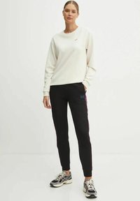 Felpa bianca con collo rotondo e branding minimale. Pantaloni jogging neri con dettagli laterali e logo. Scarpe sportive con un design testurizzato.
