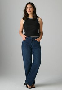 Must mustriba crop top valge ääristusega, koos kõrge vöökohaga, laia lõikega tumesiniste teksadega ning mustade plätudega.