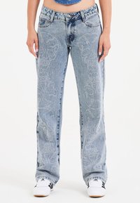 Jeans in denim azzurro con vestibilità ampia, caratterizzati da intricati motivi di teschi bianchi sui lati, design classico a cinque tasche e bottone metallico basilare.