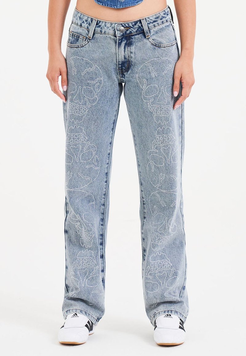 Jeans in denim azzurro con vestibilità ampia, caratterizzati da intricati motivi di teschi bianchi sui lati, design classico a cinque tasche e bottone metallico basilare.