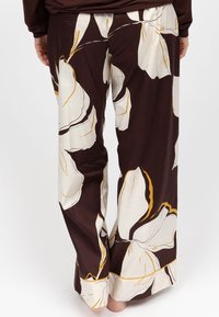 Wijde broek van lichtgewicht stof, met een bruine achtergrond en grote crèmekleurige en gele bloempatronen, en een zachte textuur.