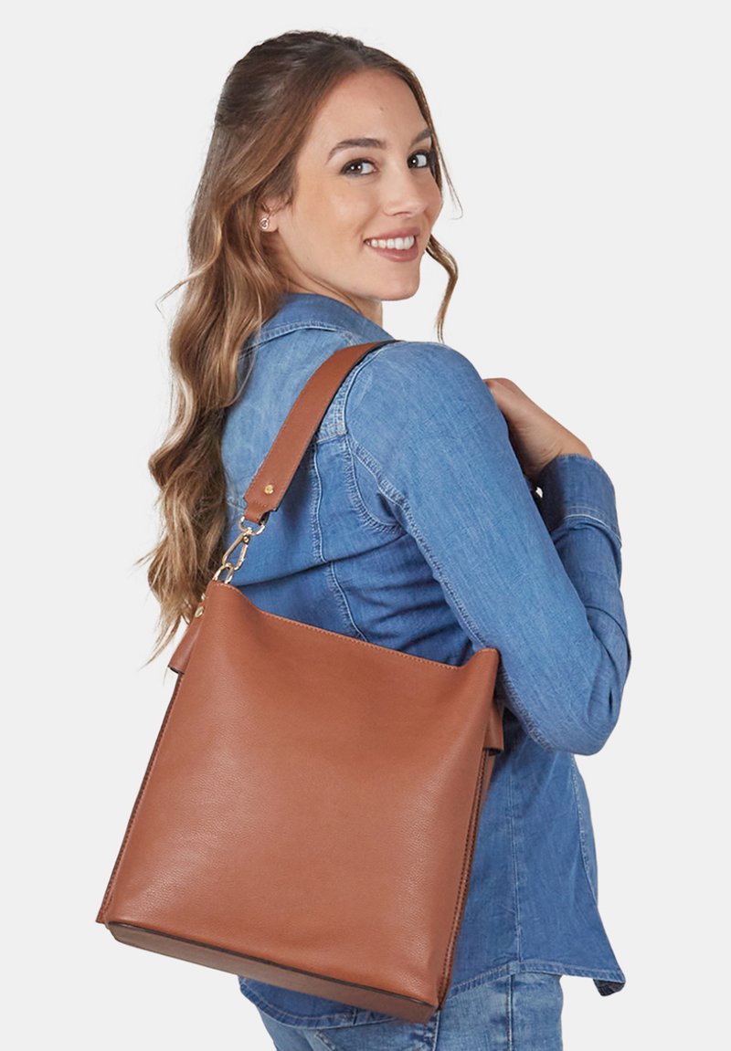 Borsa a tracolla in pelle color cuoio con una texture morbida, design minimalista e una base ampia e piatta. Presenta una tracolla staccabile con dettagli in metallo dorato.