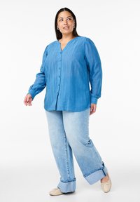 Blaues Hemd mit Knopfleiste, vertikalen Streifen, langen Ärmeln und V-Ausschnitt, kombiniert mit hellblauen weit geschnittenen Jeans und beigen Ballerinas.