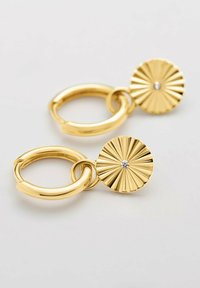 Guldtonade örhängen med en cirkulär design som har strålande linjer och en liten ädelsten i mitten. Slät metalltextur med polerad yta.