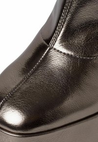 Metalowe skórzane botki sięgające kostki z eleganckim fasonem, zaokrąglonym noskiem, subtelnymi przeszyciami oraz gładką teksturą w ciemnoszarym kolorze.
