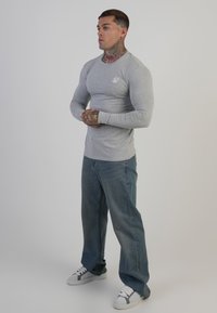 Világosszürke hosszú ujjú póló kerek nyakkal, laza kék farmernadrággal és szürke részletekkel ellátott fehér tornacipővel kombinálva.