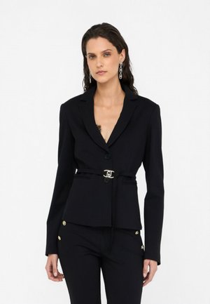 Black tailored blazer with a defined waist belt and gold-tone hardware. Features a notched lapel and long sleeves, paired with high-waisted pants.
