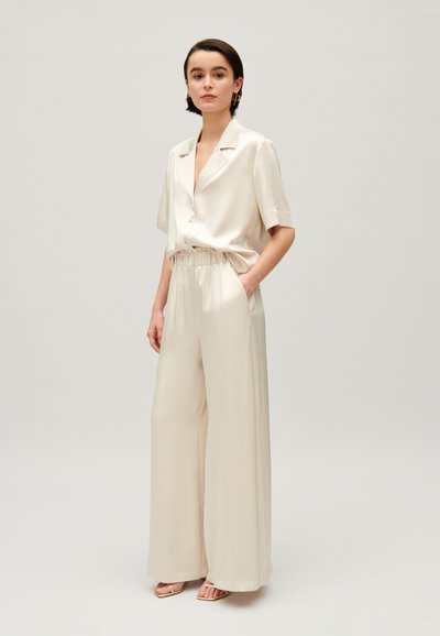 Beige skjorte med knapper og korte ermer, samt matchende vide bukser. Tøyet er glatt, og kombinerer eleganse med komfort.