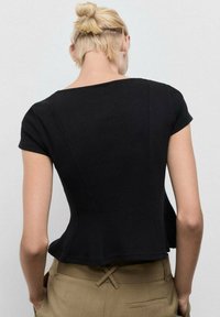 Černý přiléhavý top s krátkými rukávy, ribbovanou texturou a peplum siluetou. Má široký výstřih a čisté švy na zadní straně.