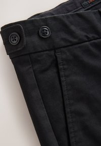 Pantalon en coton noir avec une texture lisse. Comprend deux boutons noirs à la ceinture et une finition nette et ajustée.