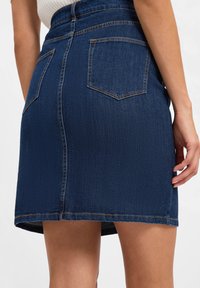 Dunkelblaßer Jeansrock mit figurbetontem Bund, zwei Gesäßtaschen, dezenten Nähakzenten und geradem Saum.