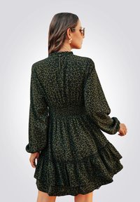 Abito verde a fantasia leopardata con maniche lunghe, vita arricciata e orlo con volants. Presenta una chiusura posteriore con bottone e un tessuto morbido e fluido.