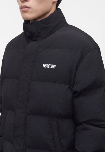 Νέος/Νέα φοράει μαύρο μπουφάν Moschino με ψηλό γιακά και εμφανές λογότυπο επωνυμίας στο στήθος.