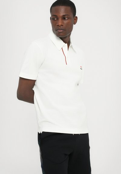 Camisola polo branca com colarinho, apresentando um acabamento em vermelho contrastante e um pequeno logótipo. Mangas curtas e um design de tecido texturizado.