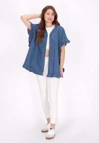 Giacca in denim stile kimono con maniche arricciate, colore azzurro chiaro, apertura frontale e orlo sfilacciato. Abbinata a jeans skinny bianchi e sneakers.