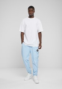 White oversized t-shirt, light blue tapered pants with a black logo patch, and white sneakers. Simple design, relaxed fit, and soft texture.