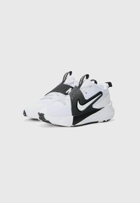 Baskets blanches avec des accents noirs, présentant un dessus texturé, un système de laçage et un logo Nike prominent sur le côté. Semelle en caoutchouc épaisse.