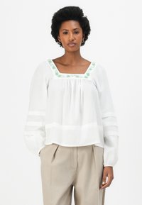 Blusa branca com mangas longas e balão, decote quadrado e desenho floral verde bordado. Apresenta riscas horizontais nas mangas e na bainha.