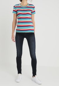 Gestreepte T-shirt in blauw, rood, groen en wit, met een ronde halslijn en korte mouwen, gecombineerd met donkere skinny jeans en witte sneakers.