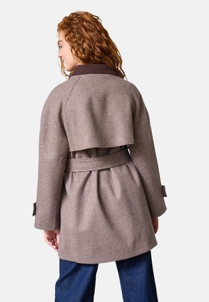 Brun uldblandingsfrakke med et lagdelt rygdesign, matchende bælte og brede ærmer. Mørk krave kontrasterer med hovedstoffets farve.