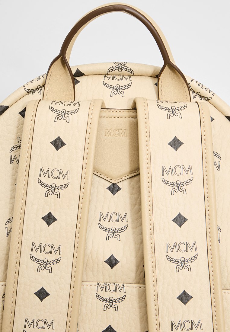 Beige Leder-Rucksack mit einem geprägten MCM-Logo-Muster, runder Form, zwei Schultergurten und einem oberen Griff zum Tragen.
