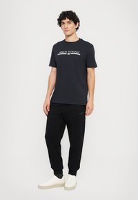 Marineblå bomulls T-skjorte med hvitt "Armani Exchange"-logo, kombinert med svarte joggebukser og hvite sneakers. Tilpasset passform og rund hals.
