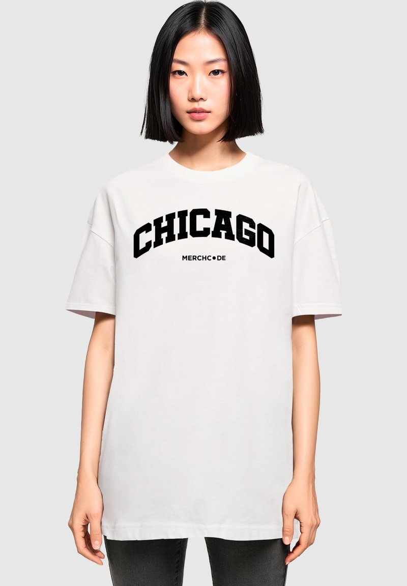 Witte oversized t-shirt met vet zwart tekst dat "CHICAGO" en "MERCH•DE" leest, korte mouwen en een ronde hals.