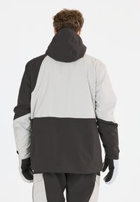 Veste imperméable avec capuche, arborant un design en blocs de couleurs noir et gris clair. Comprend un tissu texturé et des poignets élastiques.