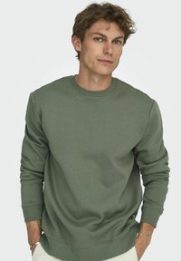 Sweatshirt à col rond olive en tissu de coton doux, présentant des poignets et un ourlet côtelés, avec une coupe décontractée.