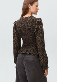 Top in stampa leopardata con maniche lunghe, corpetto arricciato e dettagli a balze sulle spalle. Indossato con pantaloni di jeans scuri a vita alta.