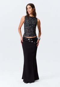 Μαύρη εφαρμοστή φούστα με φαρδύ στρίφωμα, σε συνδυασμό με αμάνικο τοπ με πολύχρωμες πουά. Αξεσουάρ περιλαμβάνει μαύρη ζώνη.