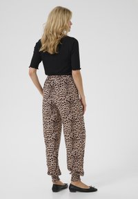 Pantaloni con stampa leopardata, dotati di vita e polsini elastici, realizzati in tessuto morbido; abbinati a una maglietta nera a maniche corte. Indossate scarpe nere senza tacco.