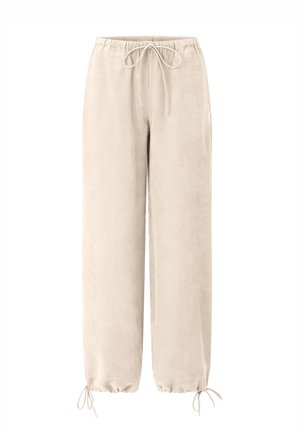 Pantaloni largi bej deschis cu talie elastică și șnururi la talie și glezne, confecționați dintr-un material moale.