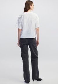 Witte kortekort mouwen top met een textuurstof en een losse pasvorm, gecombineerd met donkere grijze wijde broek en zwarte leren enkellaarzen met hak.