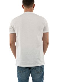 Camiseta blanca de manga corta hecha de algodón, con un diseño clásico de cuello redondo y textura sutil; combinada con jeans azules.
