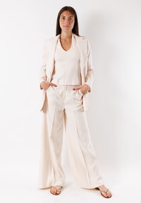 Completo beige chiaro composto da un blazer sartoriale, pantaloni a palazzo coordinati e una parte superiore aderente. Tessuto liscio con dettagli ridotti al minimo.