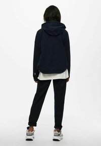 Navy fleece hooded jacket with a curved hem, paired with matching tapered pants. Features elastic cuffs and white long-sleeve layer underneath.