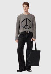 Hall halli kootud kampsun rahusümboliga, kulunud detailidega, koos mustade laiade põlvepükstega ja tekstuurse musta käekotiga. Vaatet täiendab must jalanõud.