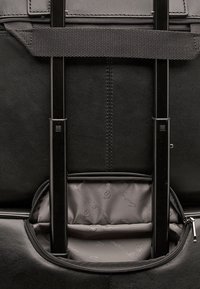 Zwarte leren reistas met dubbele rits, verstelbare schouderriem en een textuur binnendcompartiment. Inclusief twee metalen steunbalken voor stabiliteit.