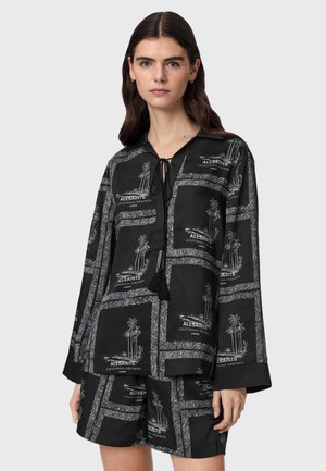 Frau trägt schwarzes, langärmeliges Hemd mit Knöpfen und passende Shorts mit weißem Palmenbaum und dem Aufdruck "AllSaints California Dreamin London".
