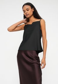 Fekete ujjatlan blúz aszimmetrikus nyakkivágással, sima, puha tapintású; burgundi selyemszoknyával párosítva.