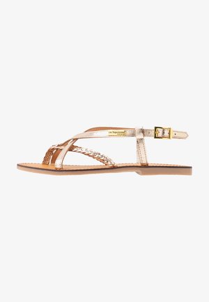 Sandalia plana metálica en oro rosa con tiras trenzadas y lisas, hebilla en el tobillo y suela color canela, marca Les Tropeziennes.