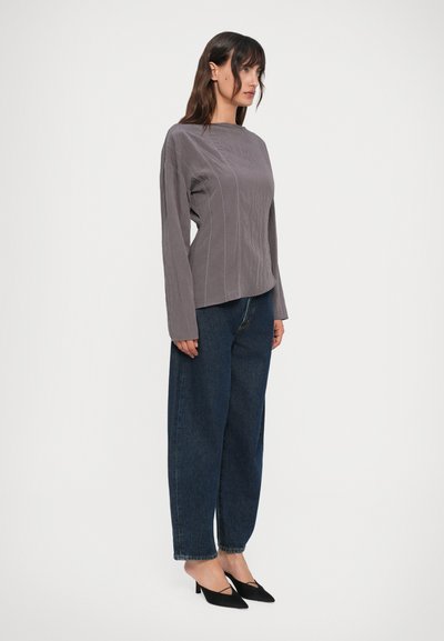 Top grigio a maniche lunghe con tessuto testurizzato e cuciture verticali, abbinato a un paio di jeans blu scuro a vita alta e scarpe nere con punta affilata.