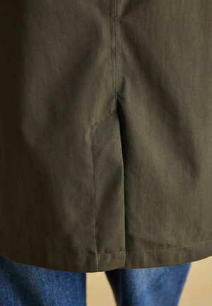 Close-up of dark olive green coat hem with back vent over blue denim jeans.