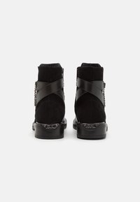 Černé kotníkové boty z semiše s hladkým koženým páskem s křížovými detaily a malým kovovým řetízkem na boku. Ploché gumové podrážky.