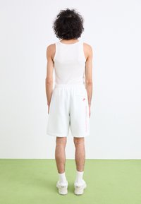 Hvide sportsshorts med et rødt Nike-logo, elastisk talje og sidelomme. Sammenklemt med en hvid tanktop samt hvide sokker og sko.
